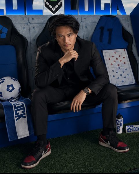 Soon F. Hoo in a black suit, seated on a blue team bench